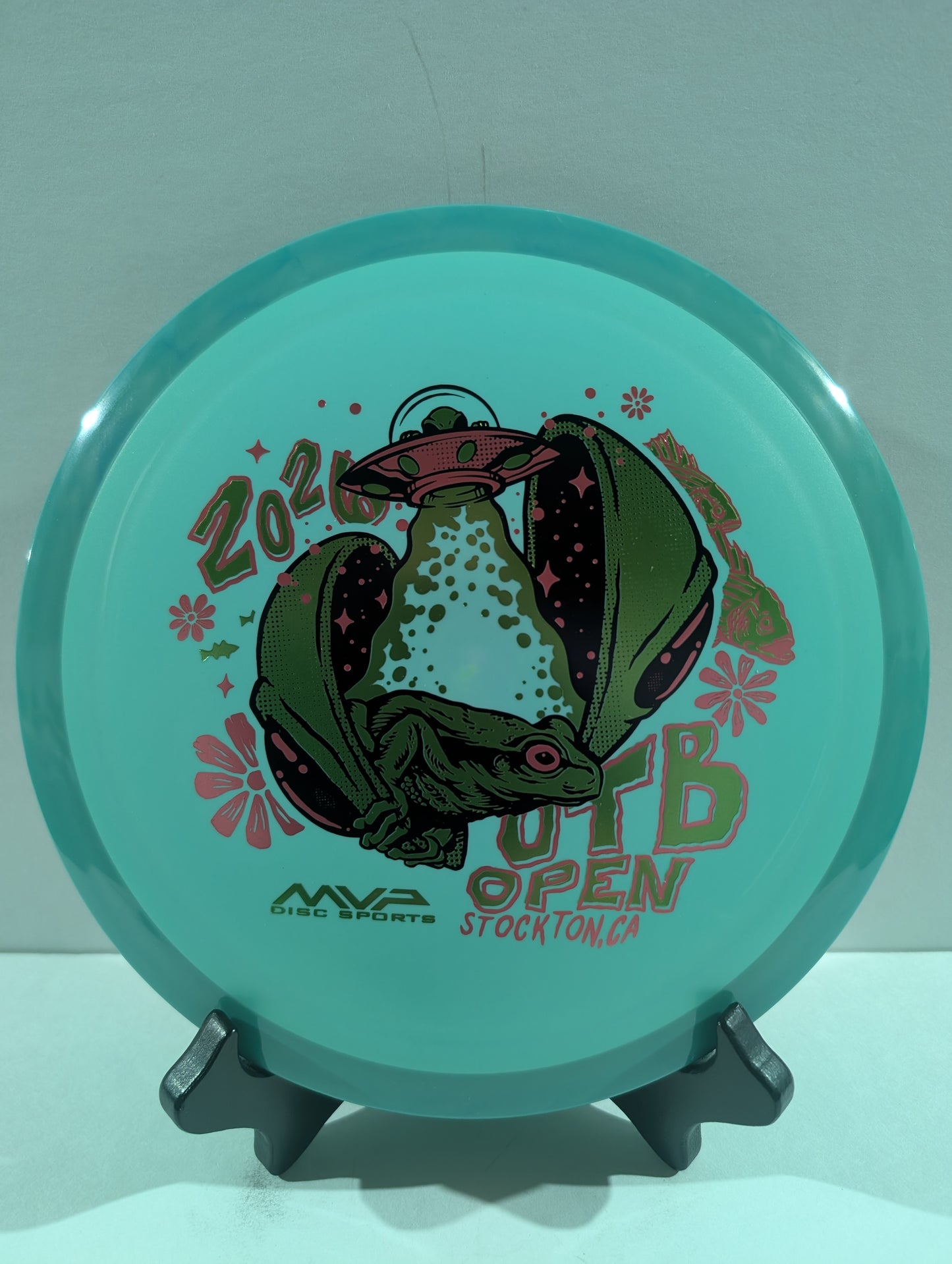 Teal disc with alien graphic and text on a stand against a light gray background