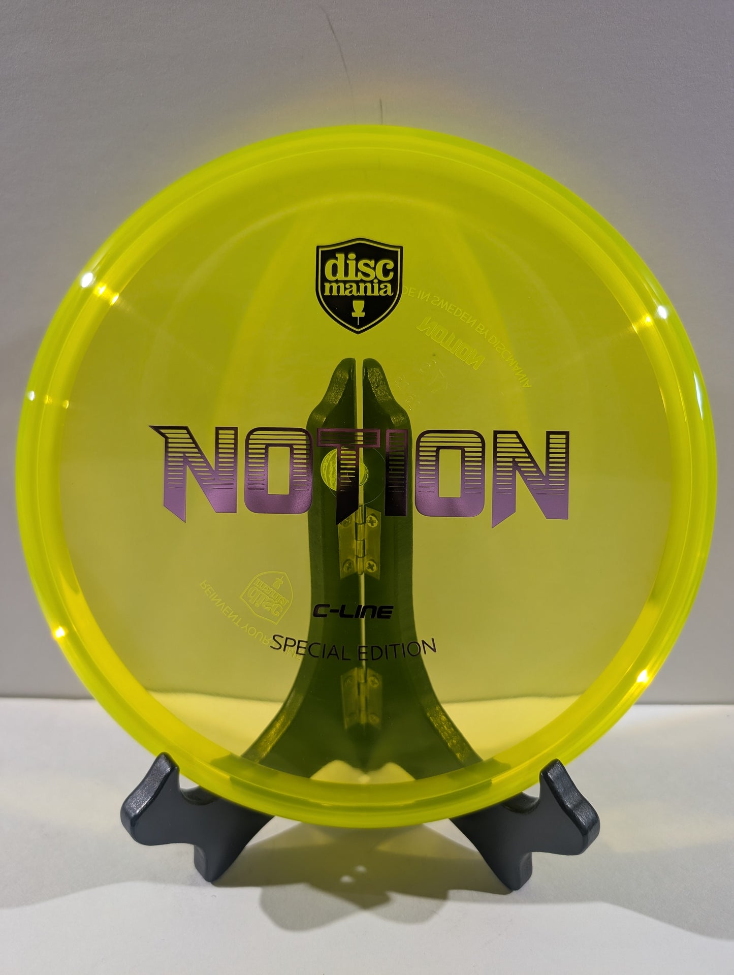 A translucent neon yellow Discmania Notion C-Line Special Edition disc golf disc displayed on a black stand against a neutral gray background.