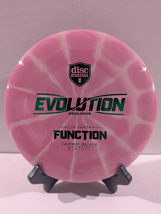 A pink swirled Discmania Evolution Lux Vapor Function fairway driver disc golf disc on a black display stand against a neutral gray background.