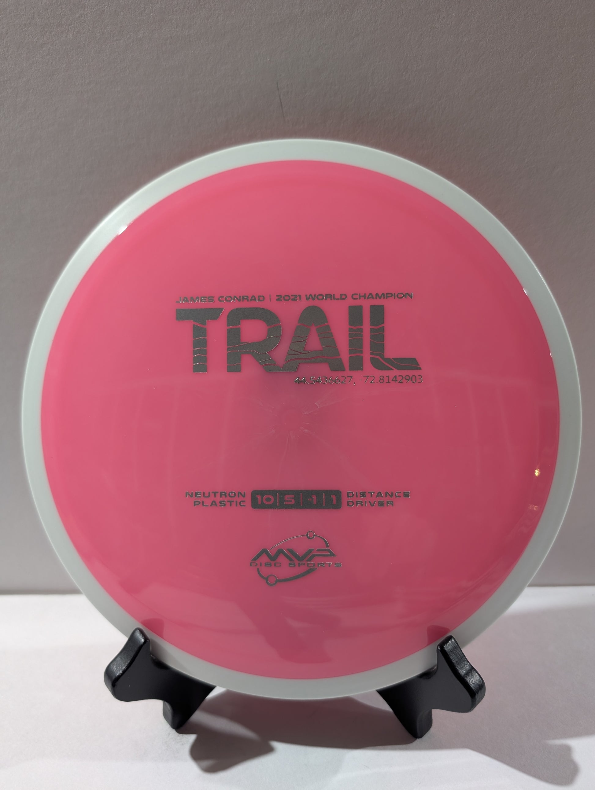Pink disc golf disc with 'Trail' branding on a stand against a neutral background