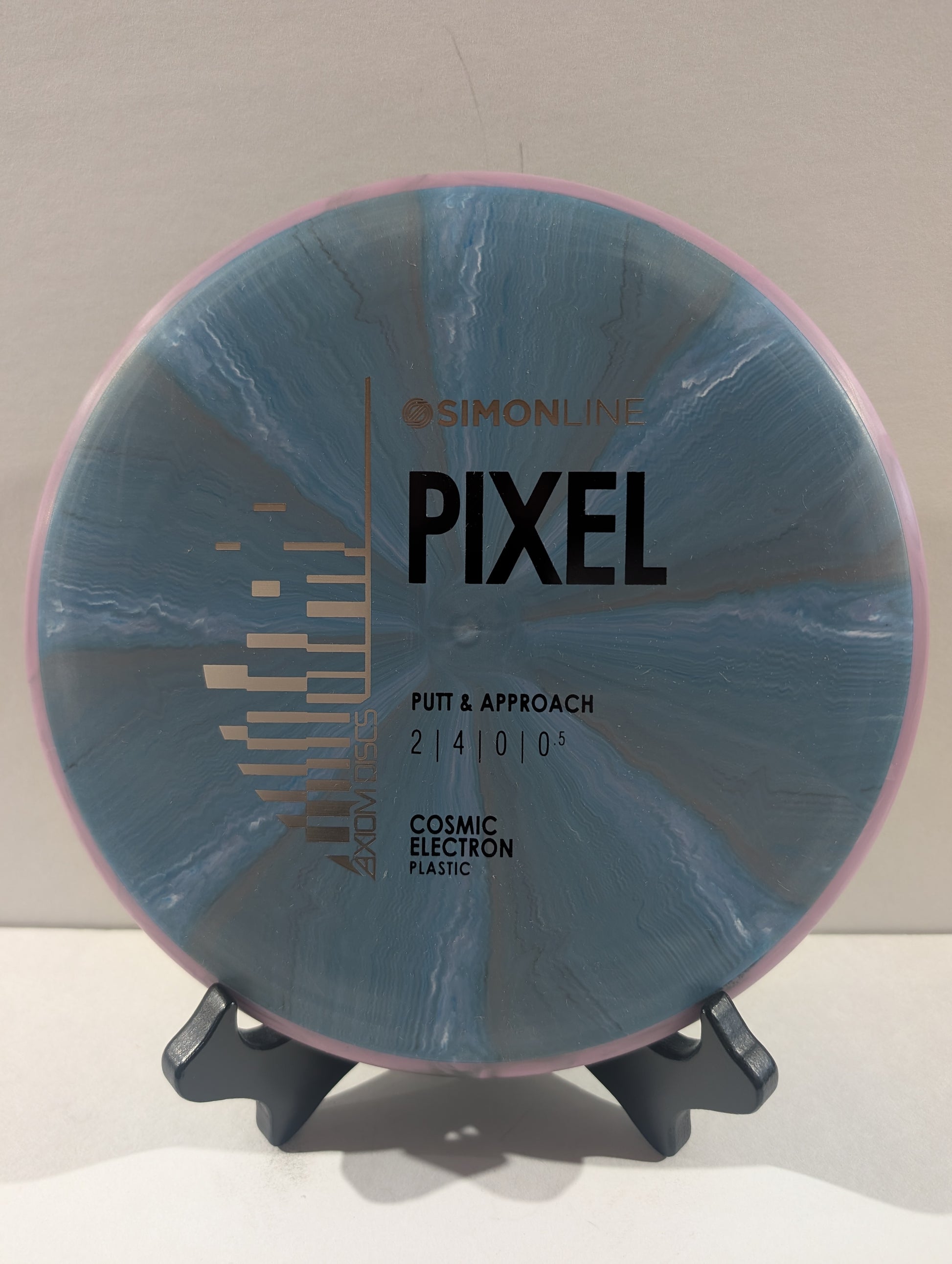 A disc golf disc on a small display stand, featuring a blue and gray marbled pattern with a pink outer rim. The disc is branded with 'Simon Line' and 'Pixel'.