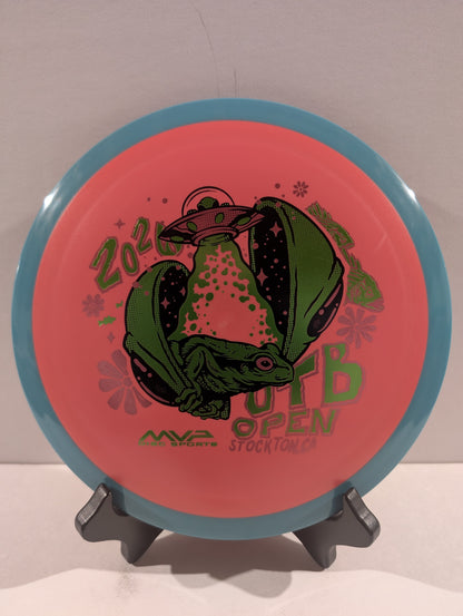 Disc golf disc with a alien graphic and text on a stand against a neutral background