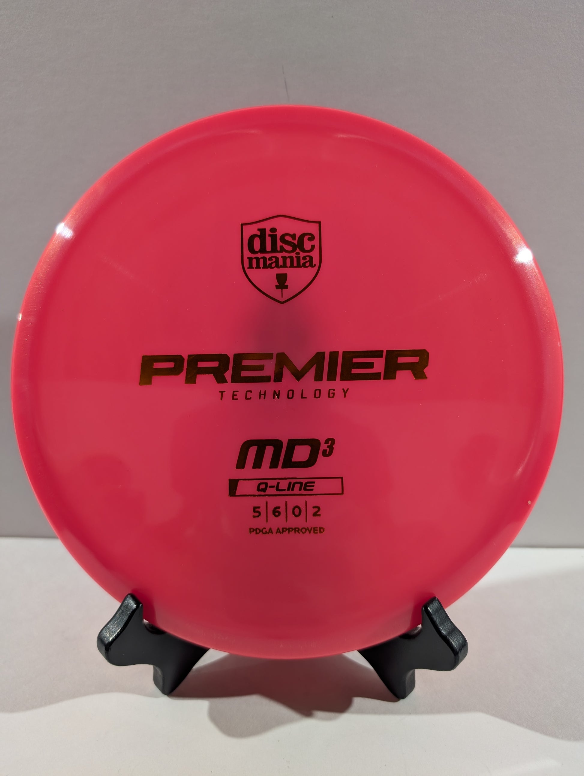 A bright pink Discmania Premier Technology MD3 Q-Line disc golf disc displayed on a small black stand against a neutral gray background.