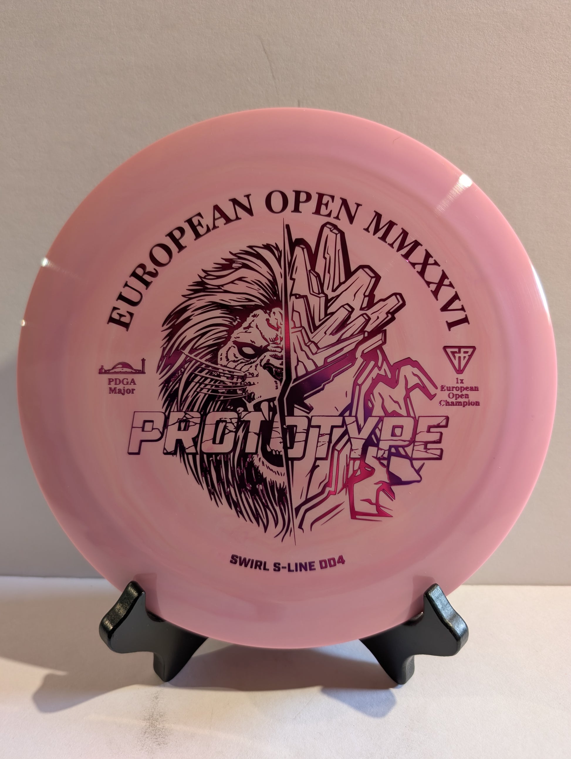 Pink disc golf disc with branding and text on a stand against a neutral background