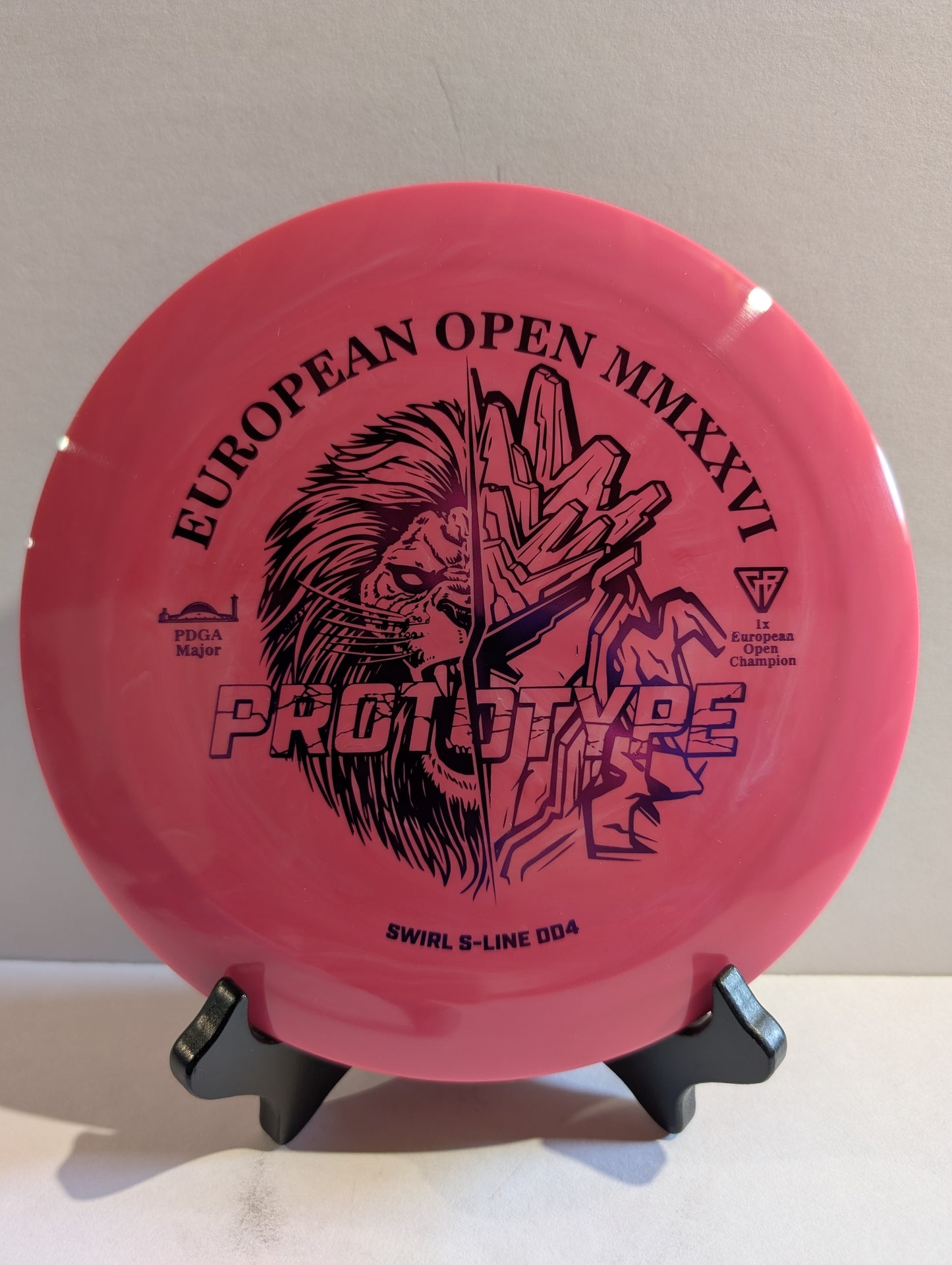 Pink disc golf disc with black graphics and text on a stand against a light background