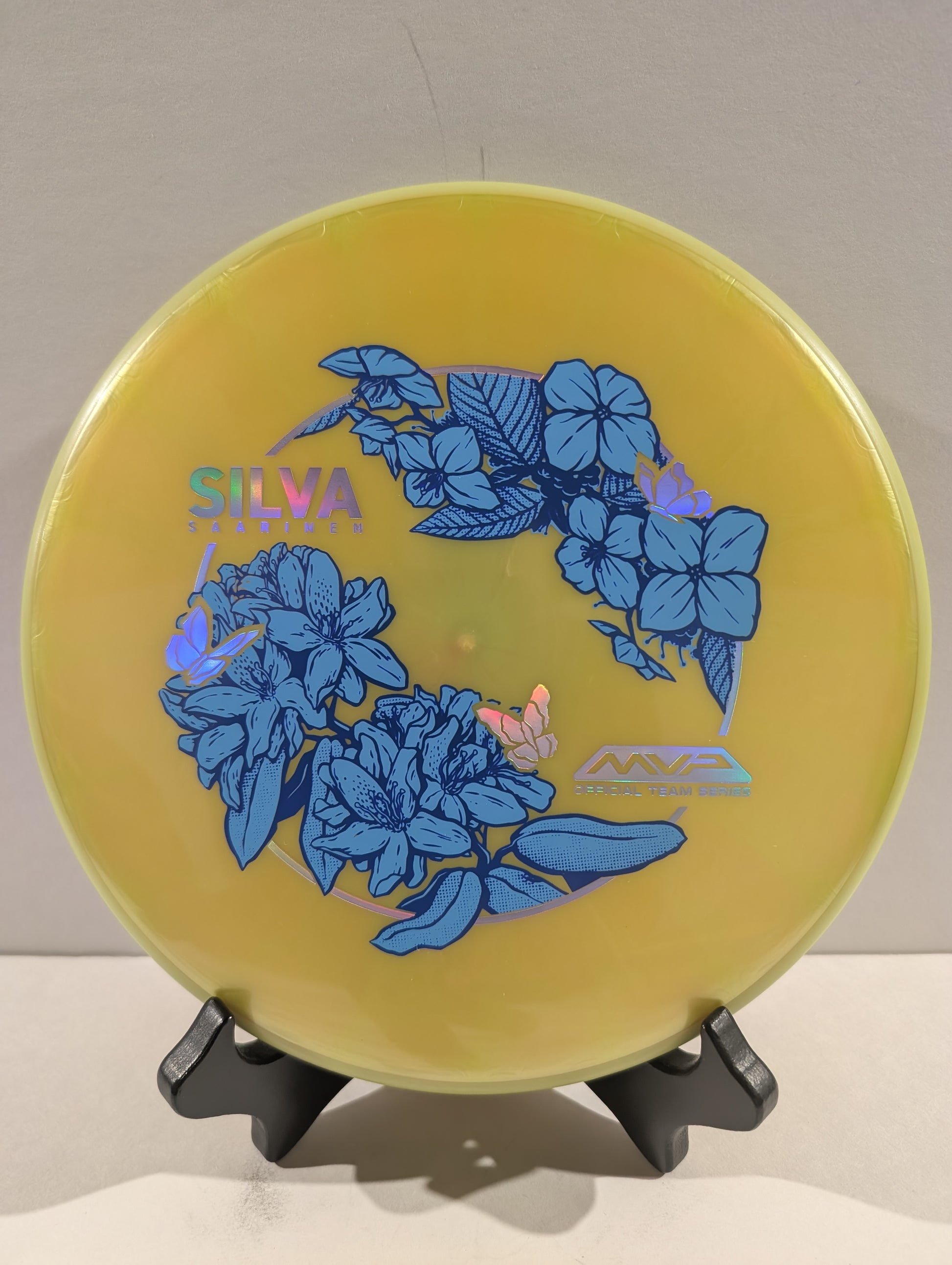 Yellow disc with blue floral design and 'Silva' branding on a stand against a neutral background