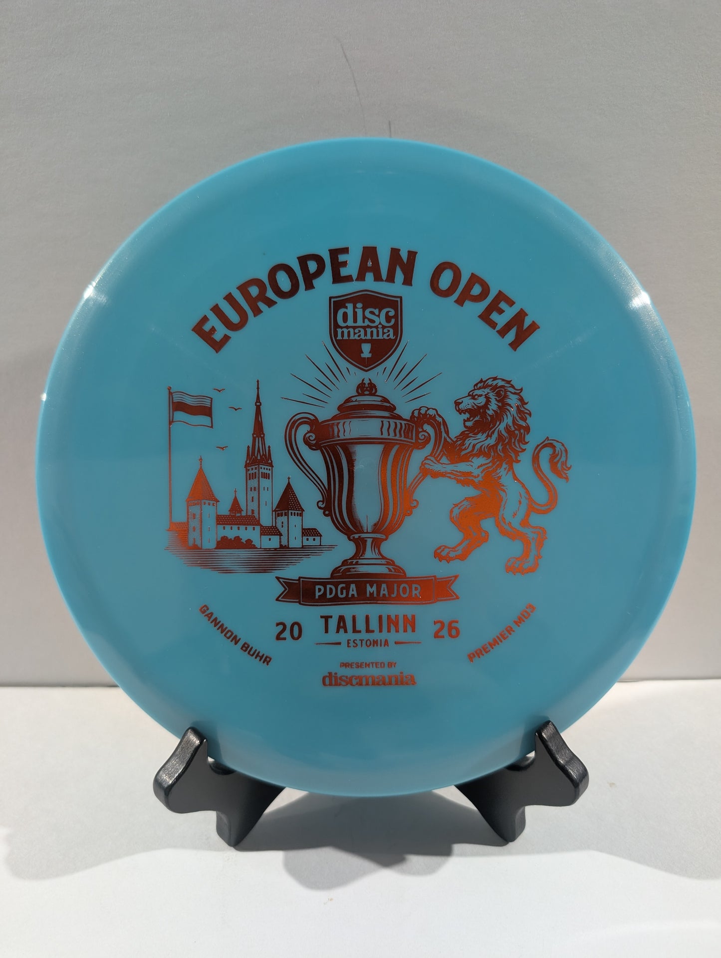 A light blue Discmania European Open disc golf disc displayed on a small black stand against a neutral light gray background.