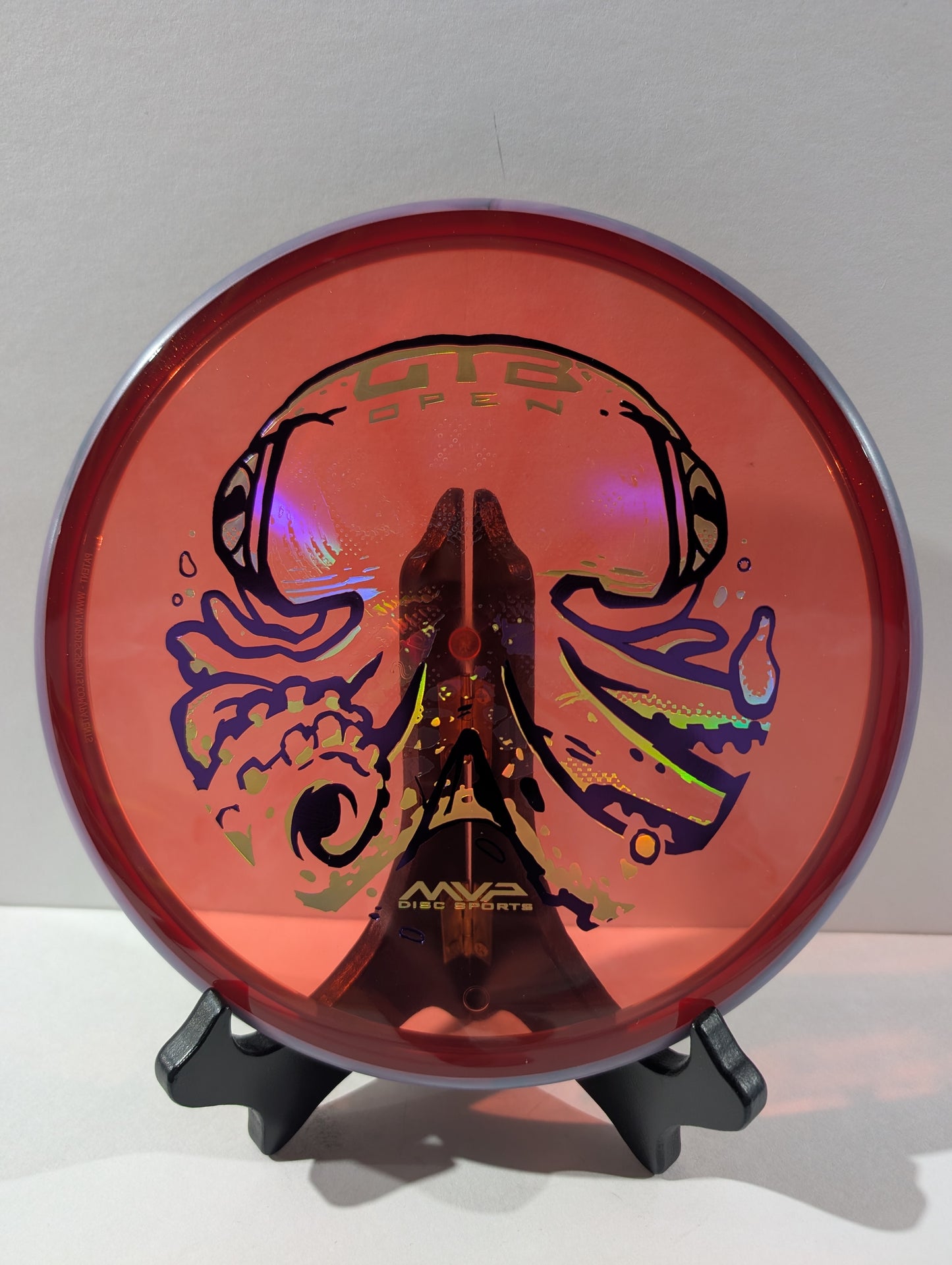 Red disc golf disc with colorful design on a stand against a gray background