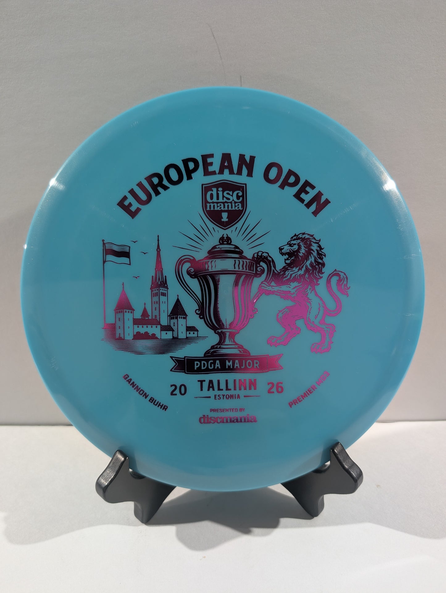 A light blue Discmania European Open disc golf disc displayed on a small black stand against a neutral light gray background.