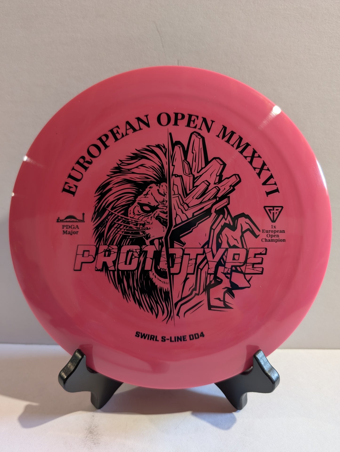 Pink disc golf disc with black text and graphics on a stand against a beige background