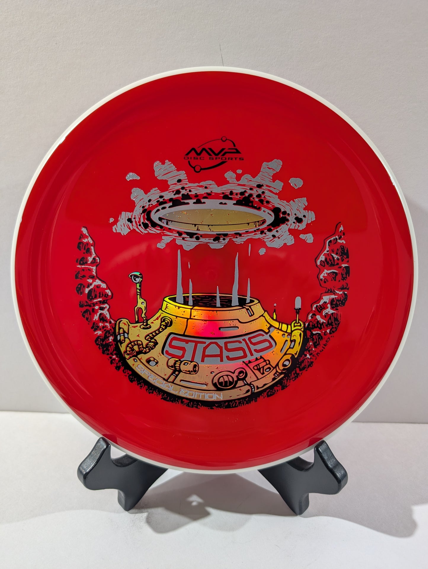Red disc with 'Stasis' design on a stand against a white background