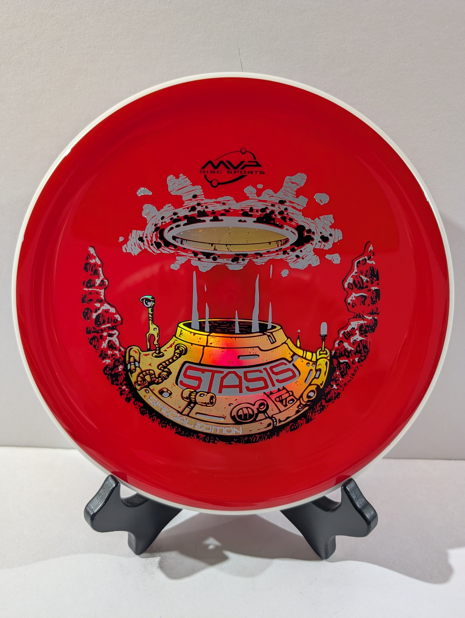 Red disc with 'Stasis' design on a stand against a white background
