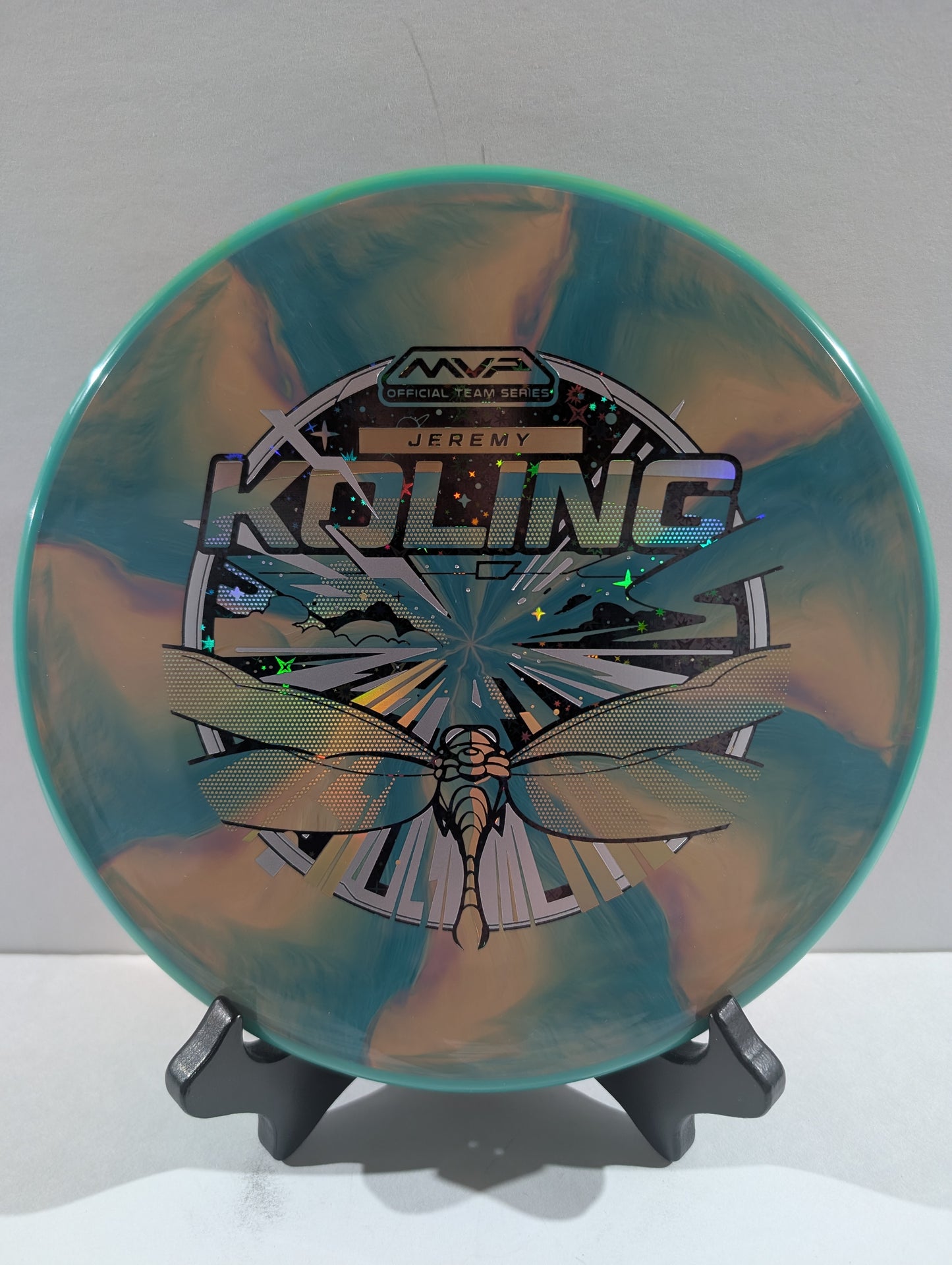 Disc golf disc with dragonfly design and branding on a stand against a white background