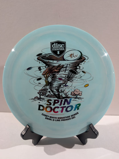 A light blue Discmania 'Spin Doctor' disc golf disc displayed on a black stand against a neutral beige background.