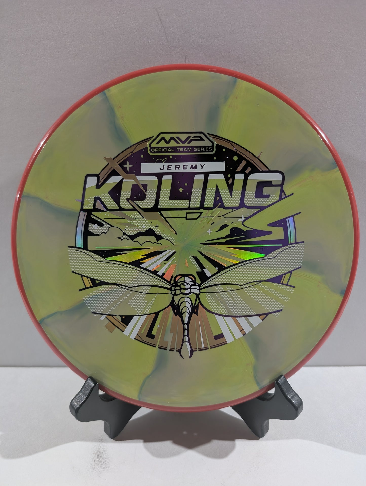 Disc golf disc with a dragonfly design and branding on a stand against a white background