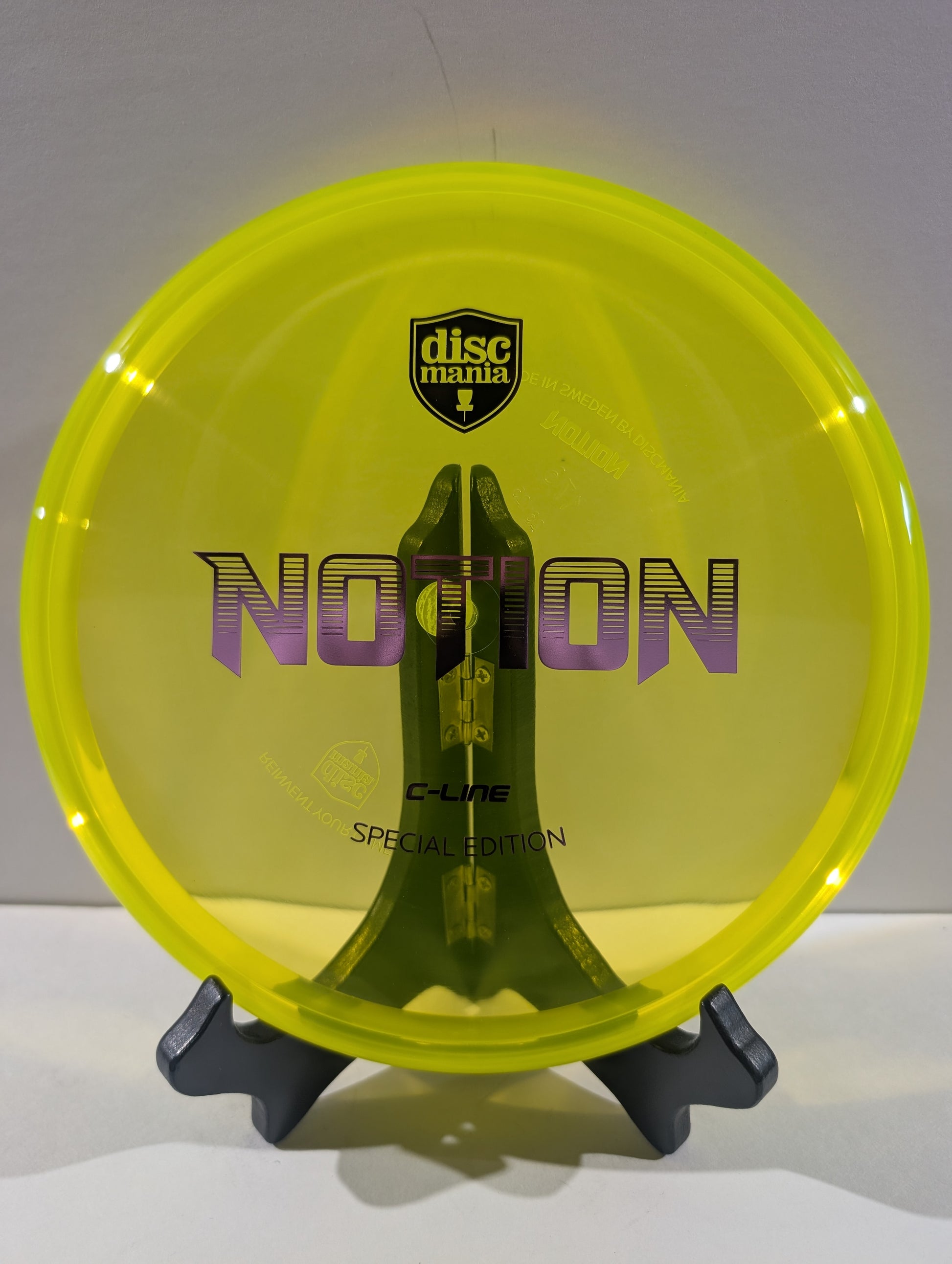 A translucent neon yellow Discmania Notion C-Line Special Edition disc golf disc displayed on a black stand against a neutral gray background.