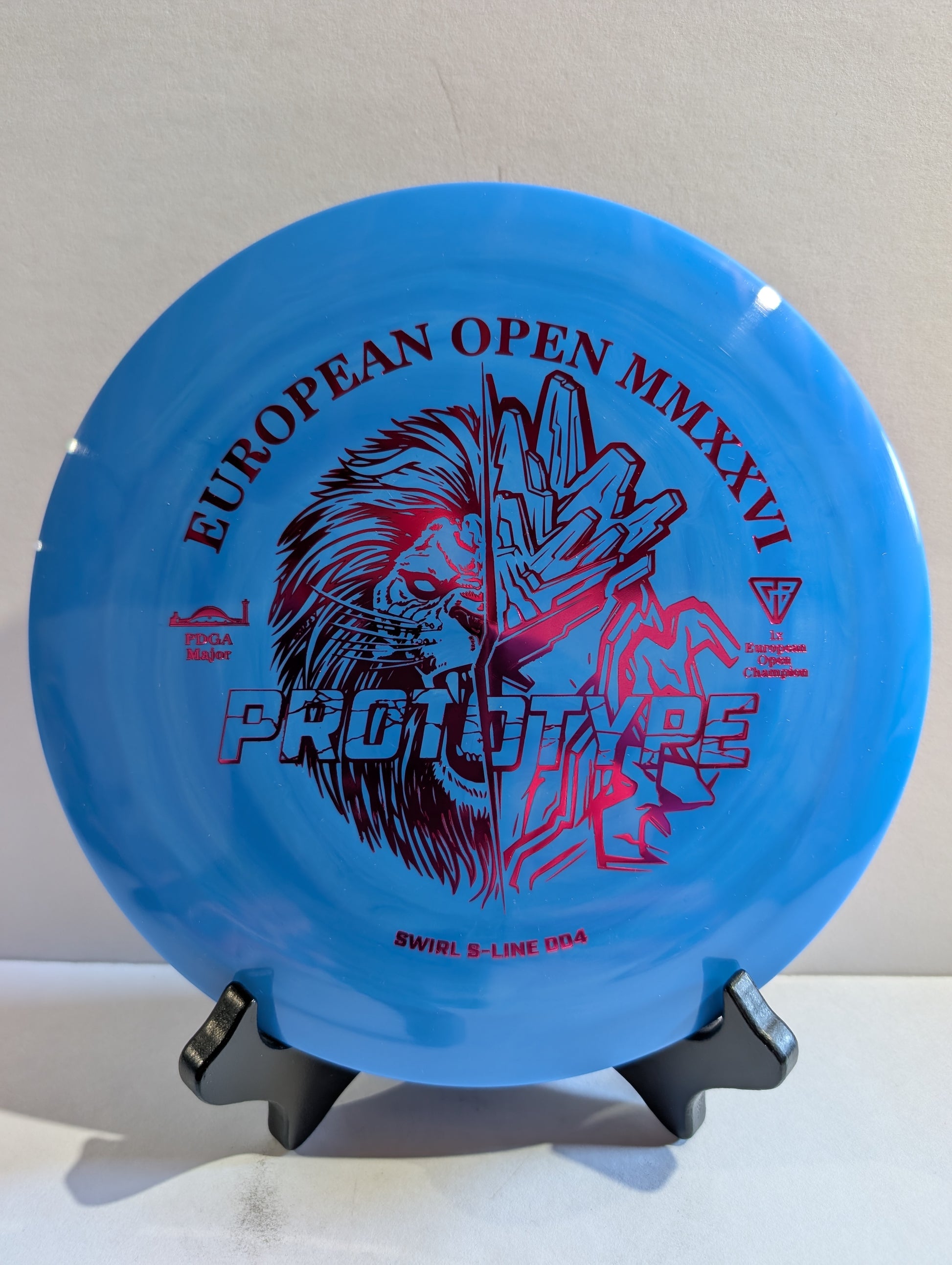 Blue disc golf disc with red and black graphics on a stand against a light gray background