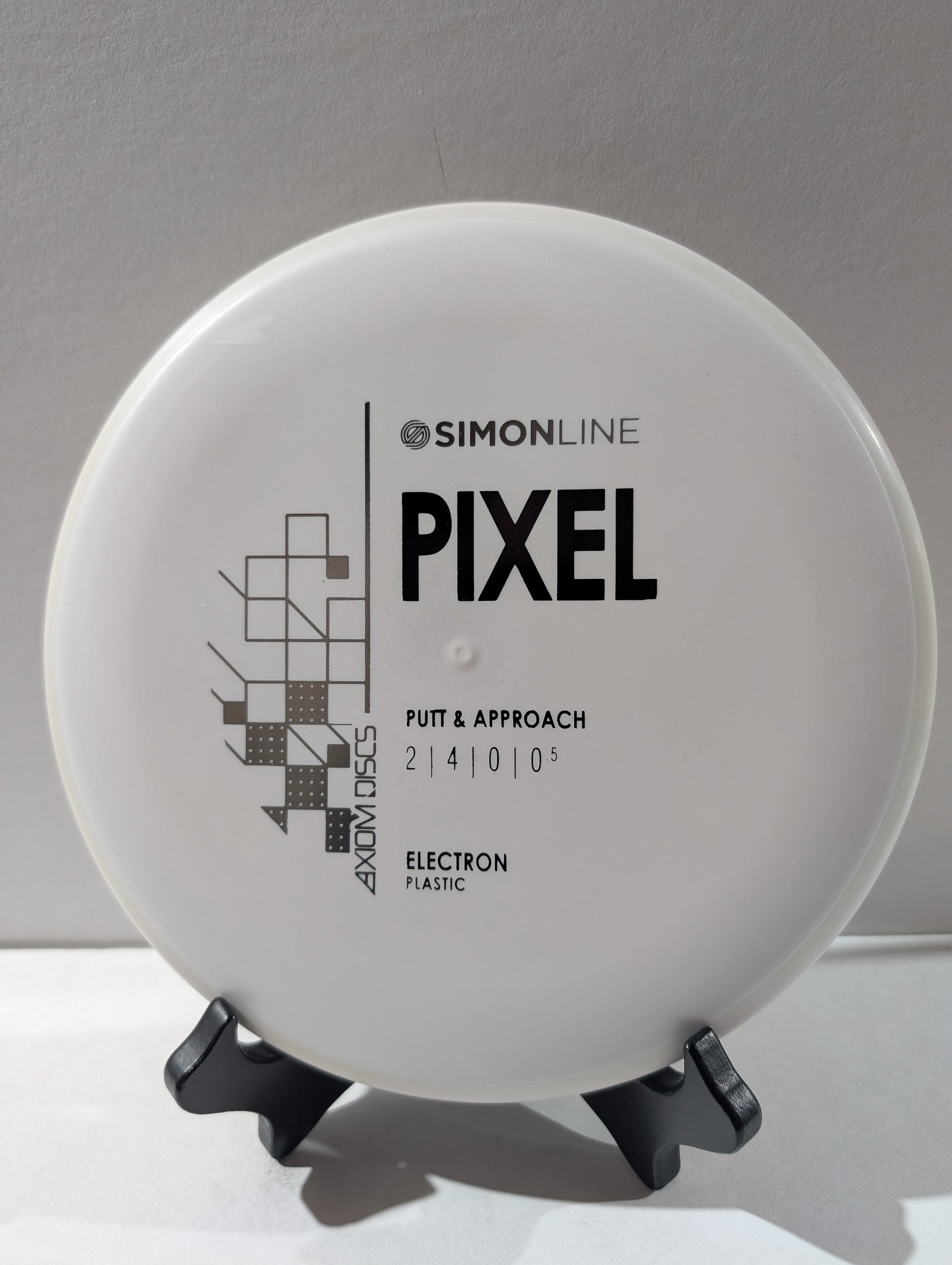 Disc golf disc with 'Simonline Pixel' branding on a stand against a neutral background