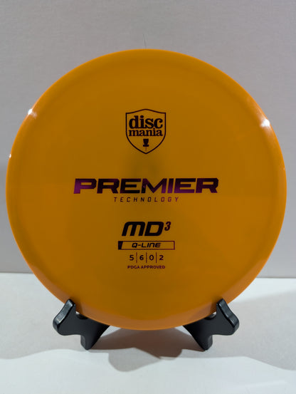 An orange Discmania Premier Technology MD3 golf disc on a small black display stand against a neutral gray background.