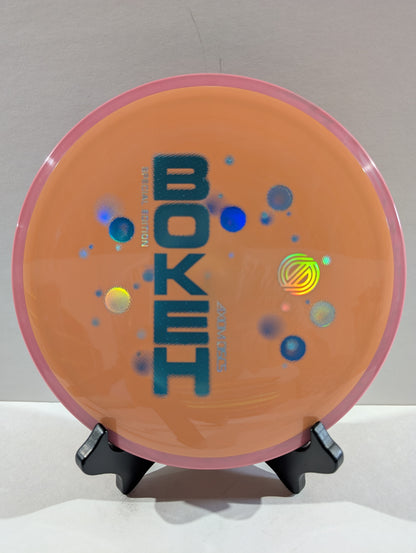 Disc golf disc with 'Bokeh' branding on a stand against a neutral background