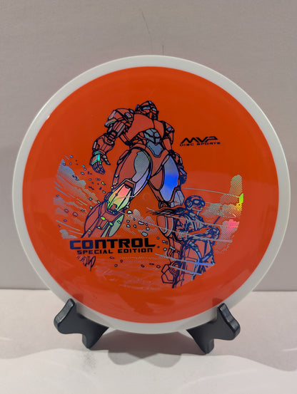 An orange disc golf disc with a white rim, featuring a graphic of a robot and the text 'CONTROL SPECIAL EDITION' and 'MVP Disc Sports', displayed on a small black stand against a neutral background.