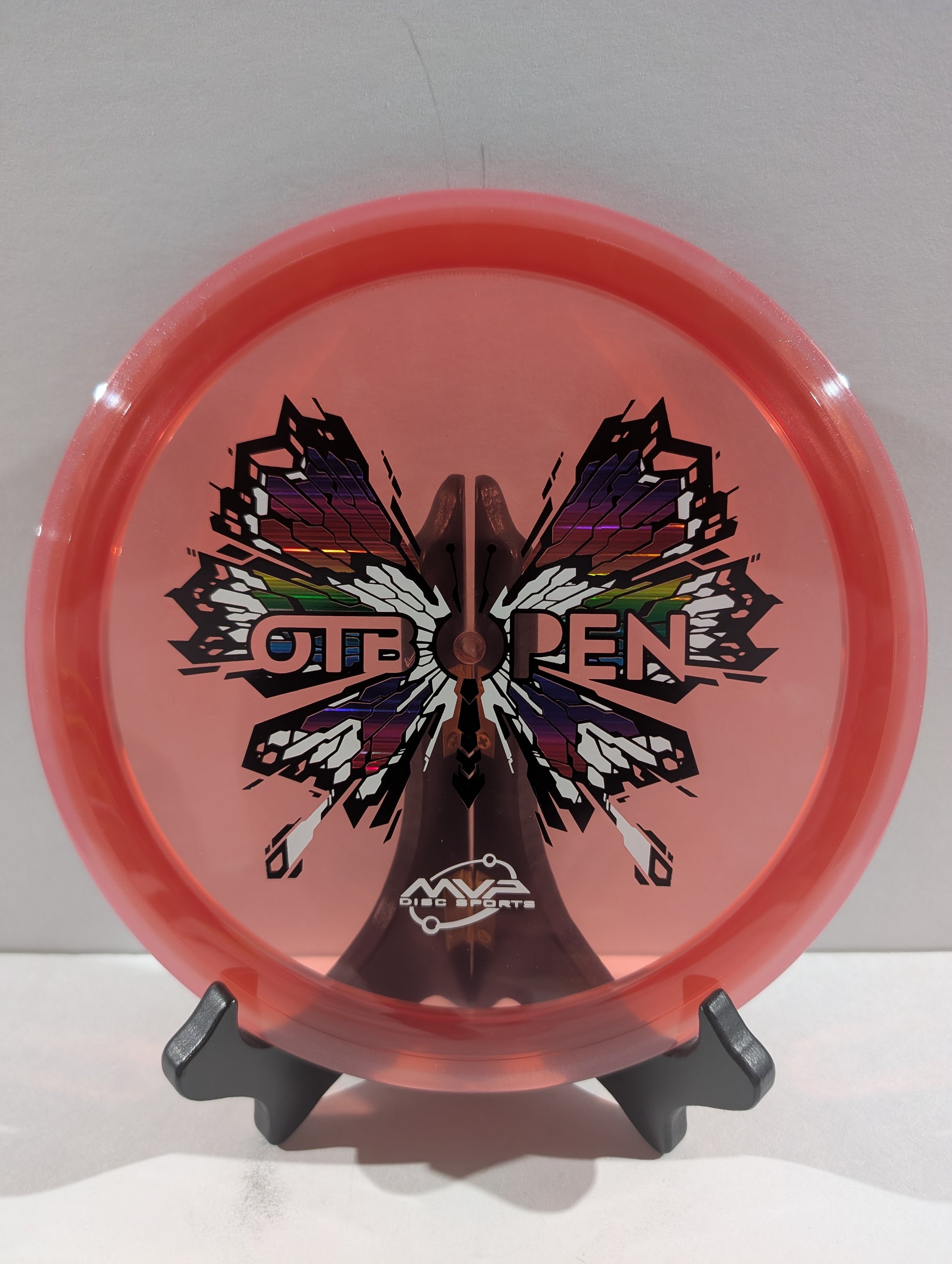 Pink disc with butterfly design and 'OTB Open' text on a stand against a white background