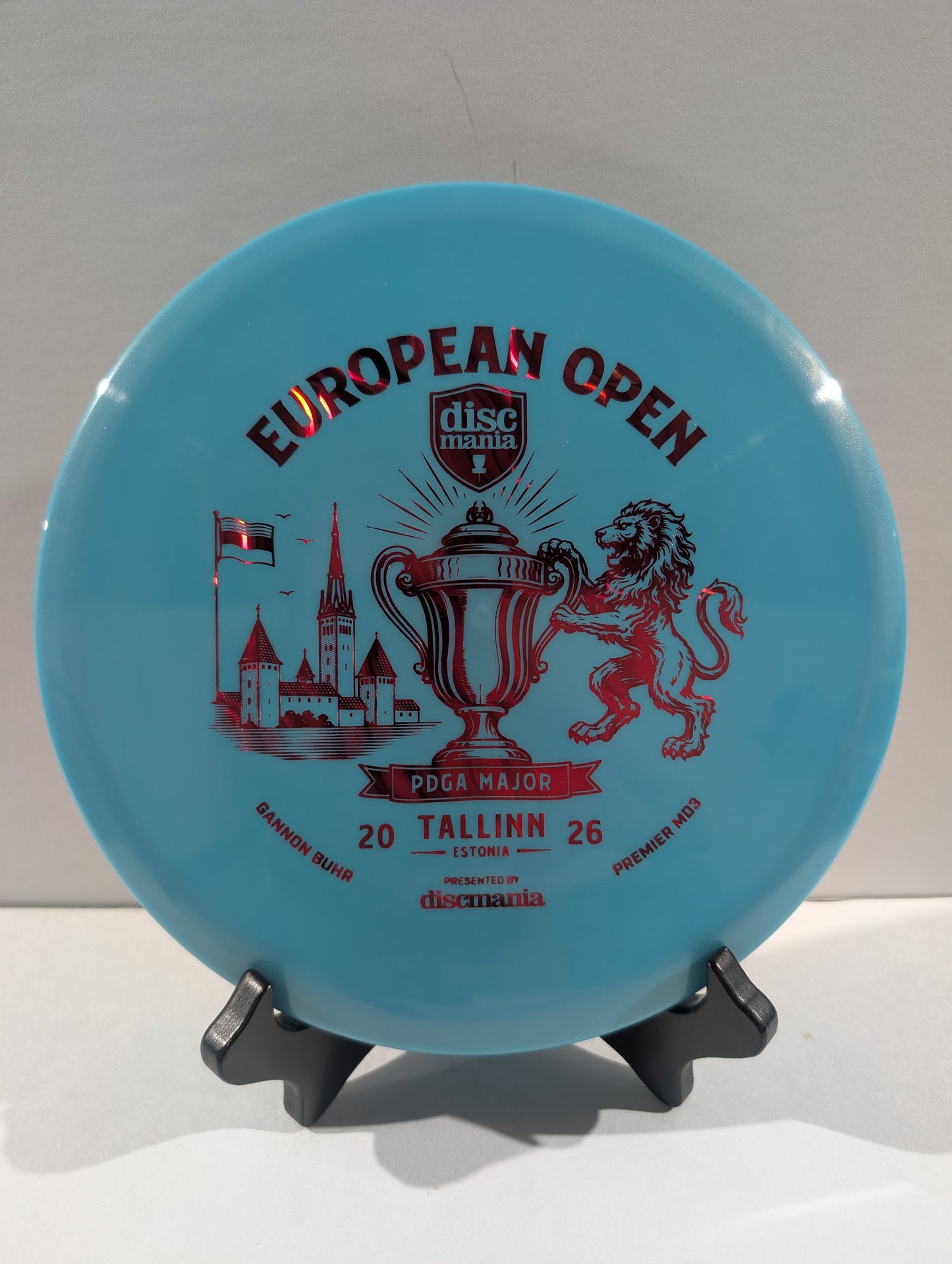A light blue Discmania European Open disc golf disc displayed on a small black stand against a neutral light gray background.