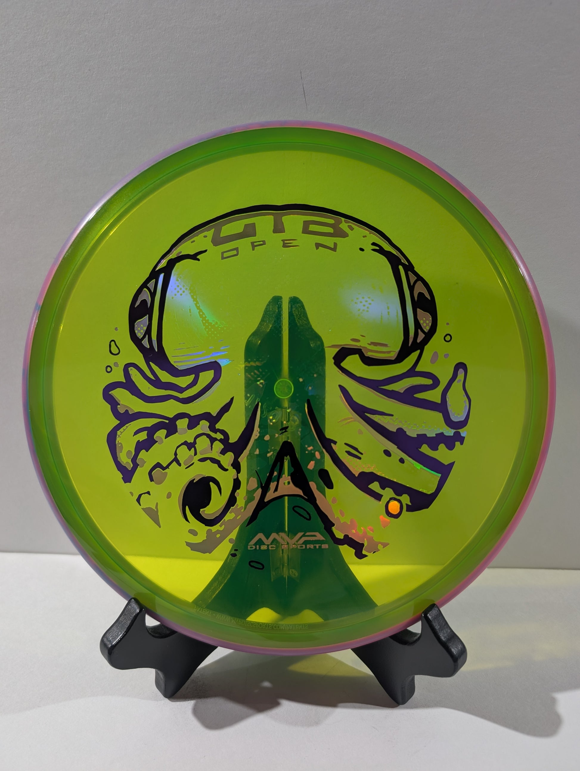 Green disc golf disc with purple and design on a stand against a gray background