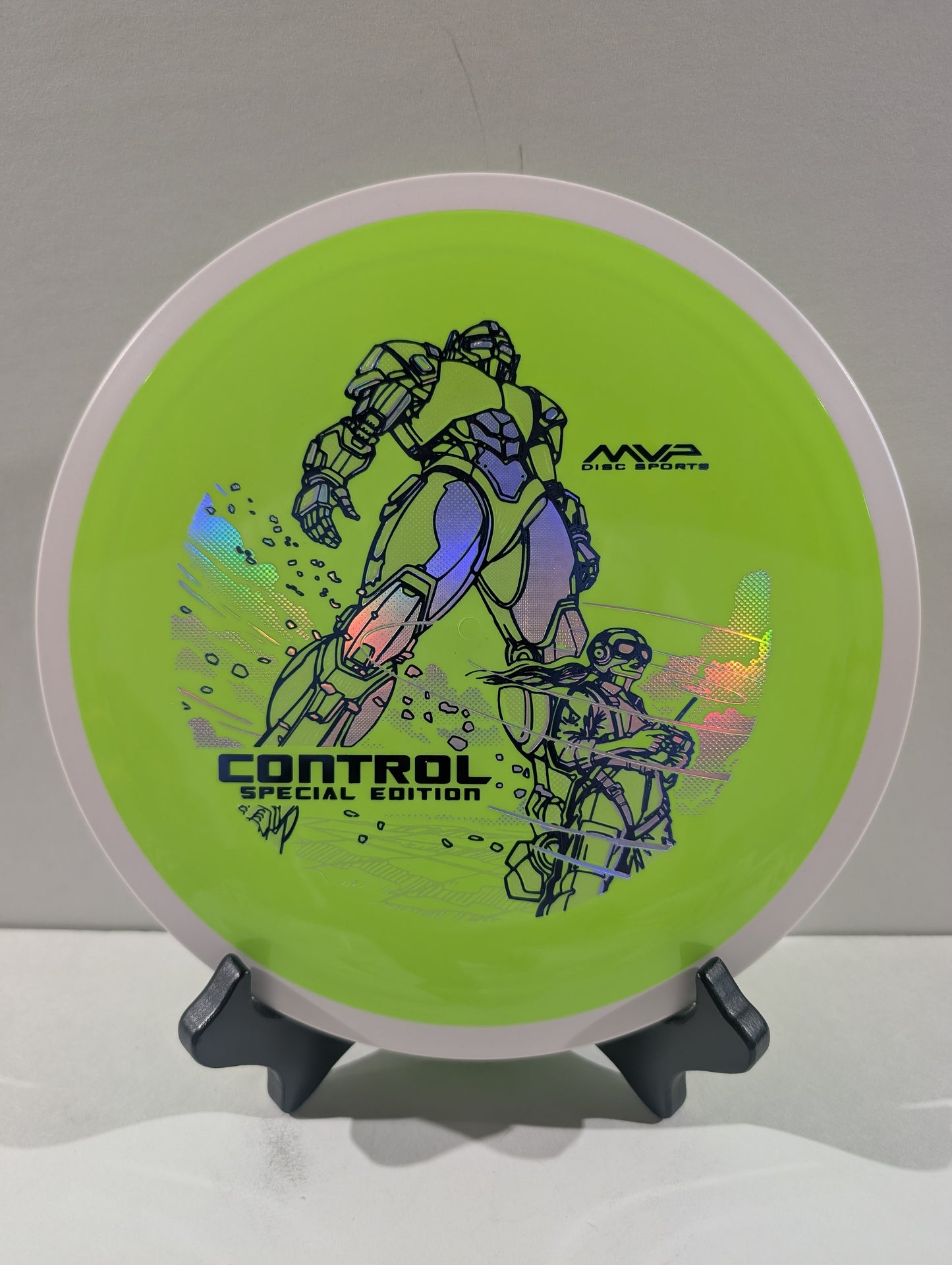 A disc golf disc on a small display stand, featuring a bright lime green background with black graphic illustrations of mecha robots and the text 'CONTROL SPECIAL EDITION' and 'MVP Disc Sports'.