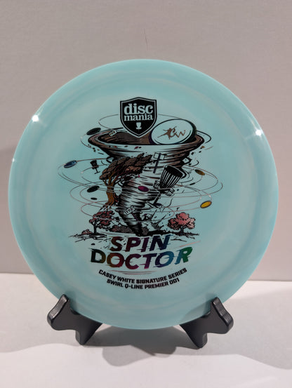 A light blue Discmania 'Spin Doctor' flying disc displayed on a black stand against a neutral gray background.