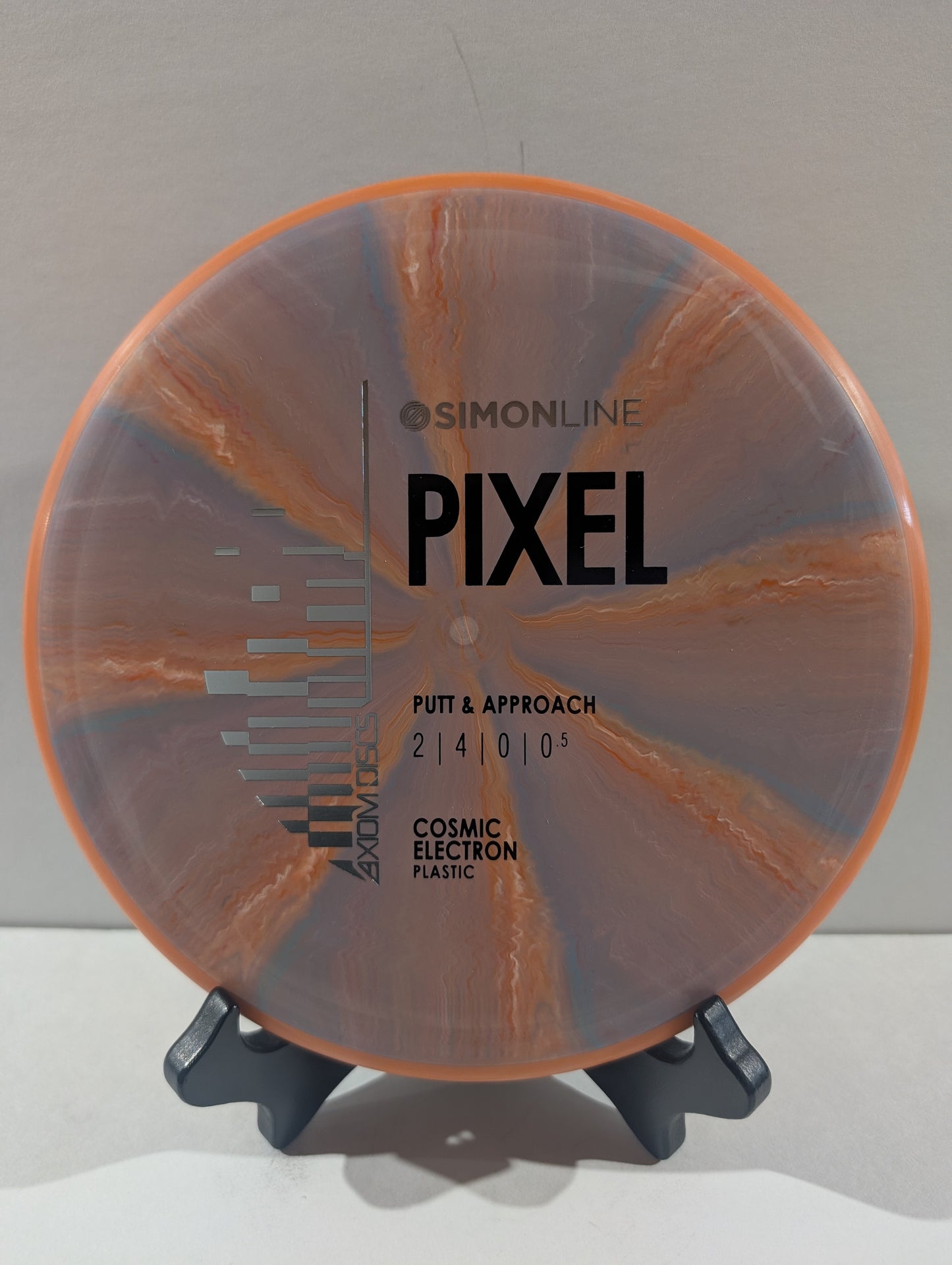 A disc golf disc on a small display stand, featuring an orange rim and a marbled pink and  orange flight plate with black printed text.