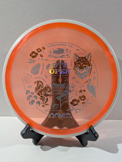 Orange disc golf disc with MVP Disc Sports branding and graphics on a stand against a gray background