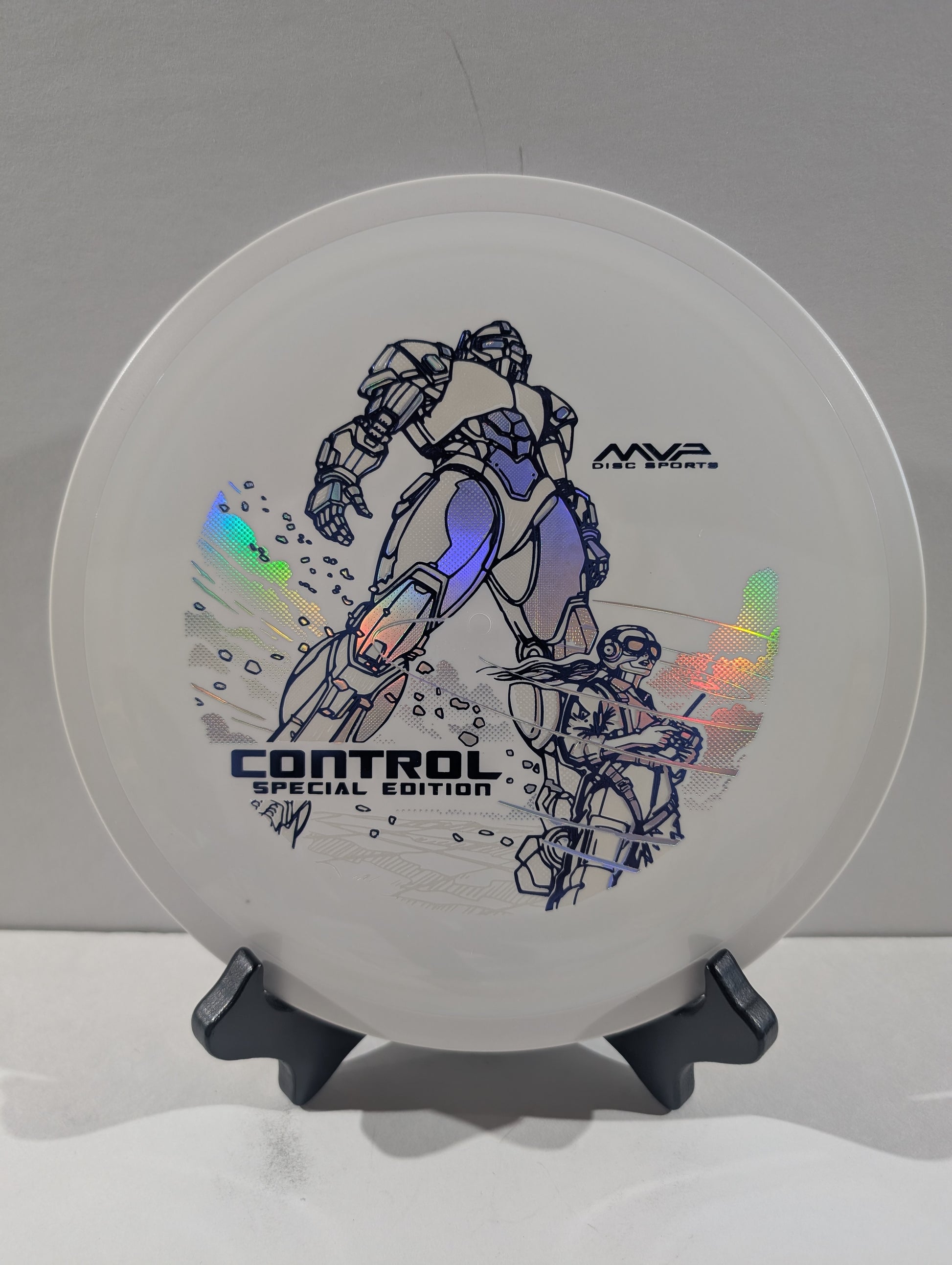 A white disc golf disc with a blue and black robot graphic, displayed on a black stand against a neutral gray background. The disc features holographic foil accents and text reading 'CONTROL SPECIAL EDITION' and 'MVP DISC SPORTS'.