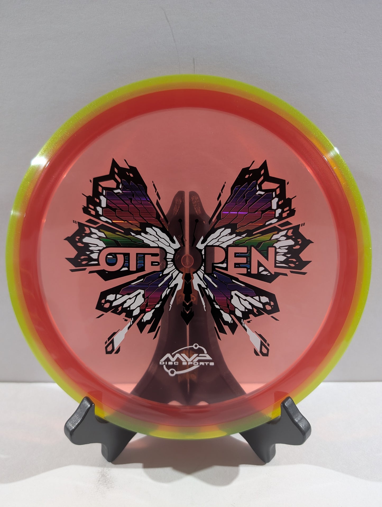 Disc with butterfly design and 'OTB Open' branding on a stand against a white background
