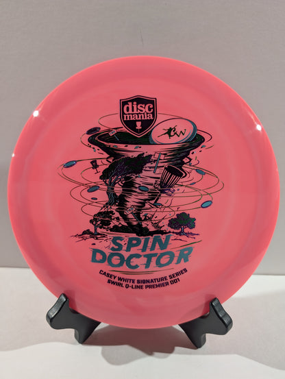A pink Discmania 'Spin Doctor' disc golf disc displayed on a black stand against a neutral gray background.