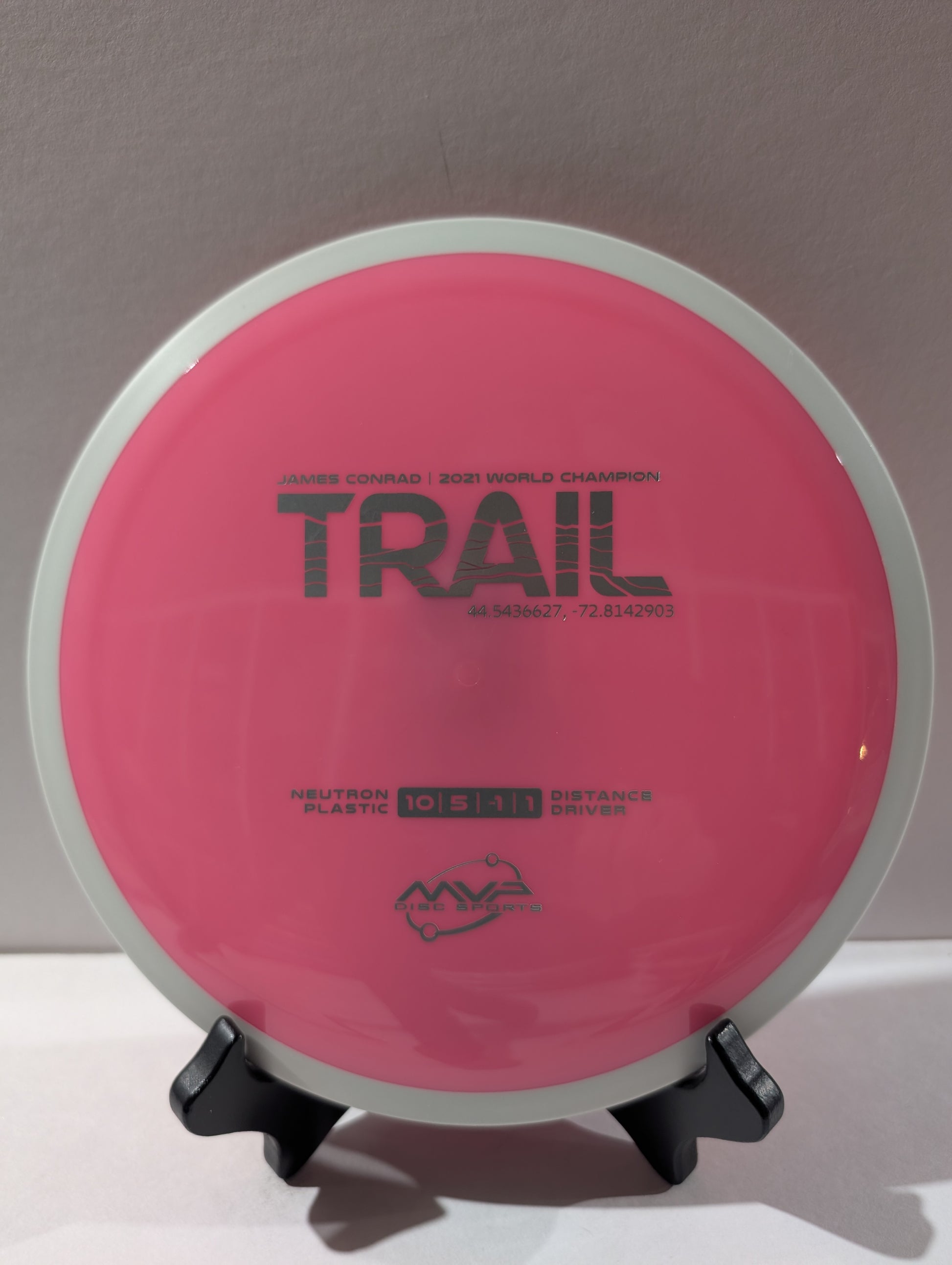 Pink disc golf disc with 'Trail' branding on a stand against a neutral background