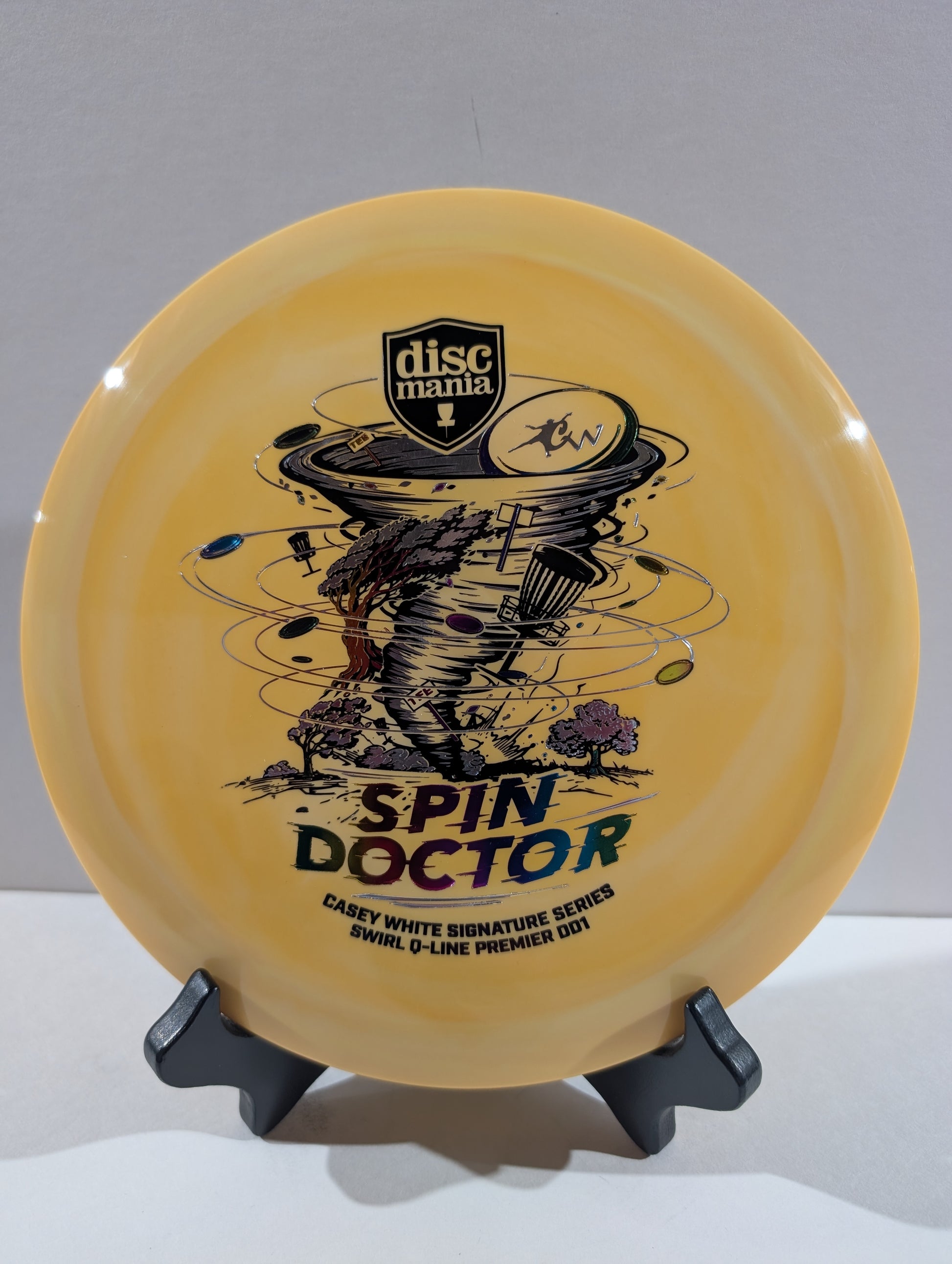 An orange Discmania Spin Doctor disc golf disc displayed on a black stand against a neutral gray background.