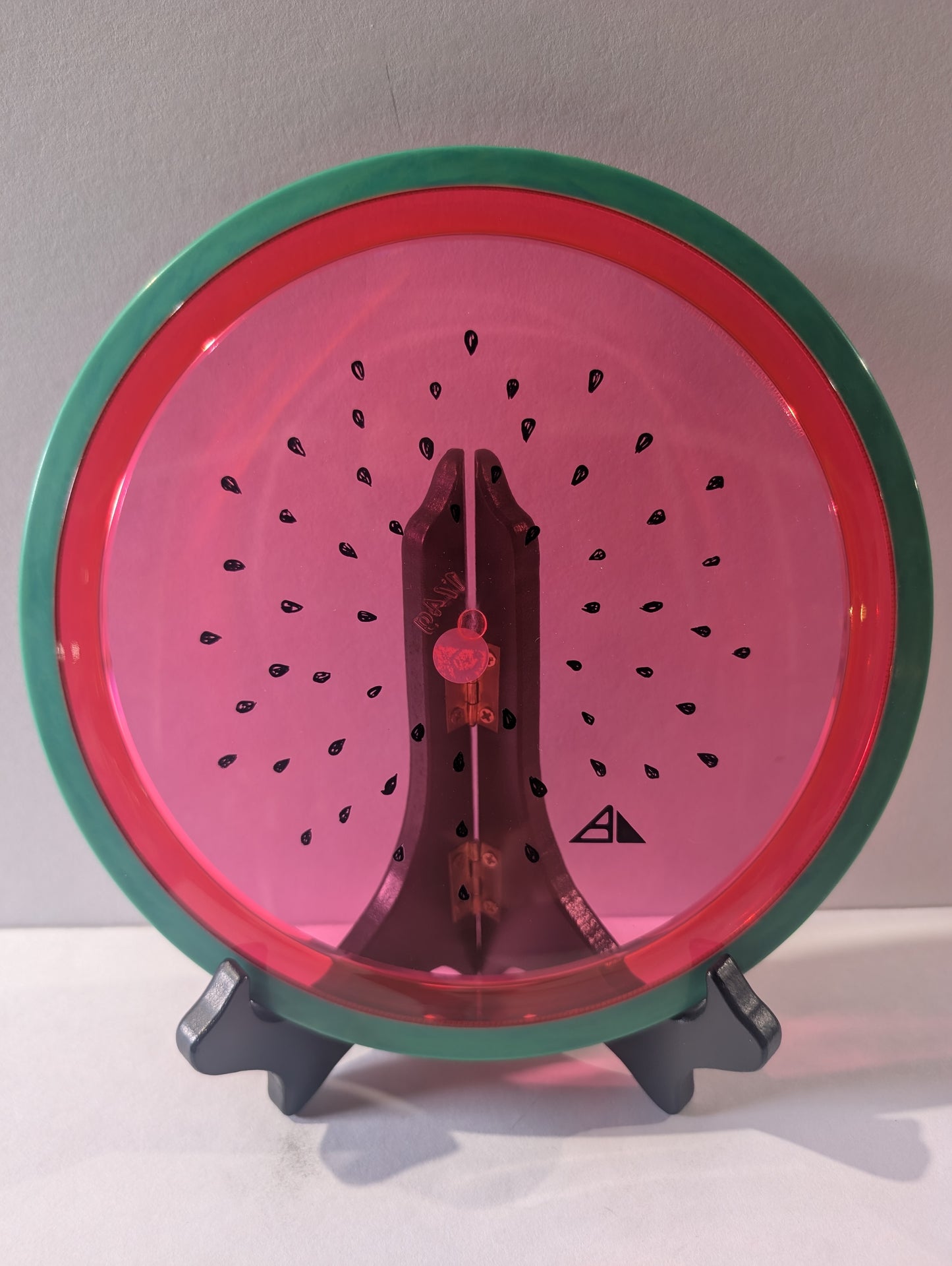 Watermelon disc colored like a watermelon with a stand on a plain background