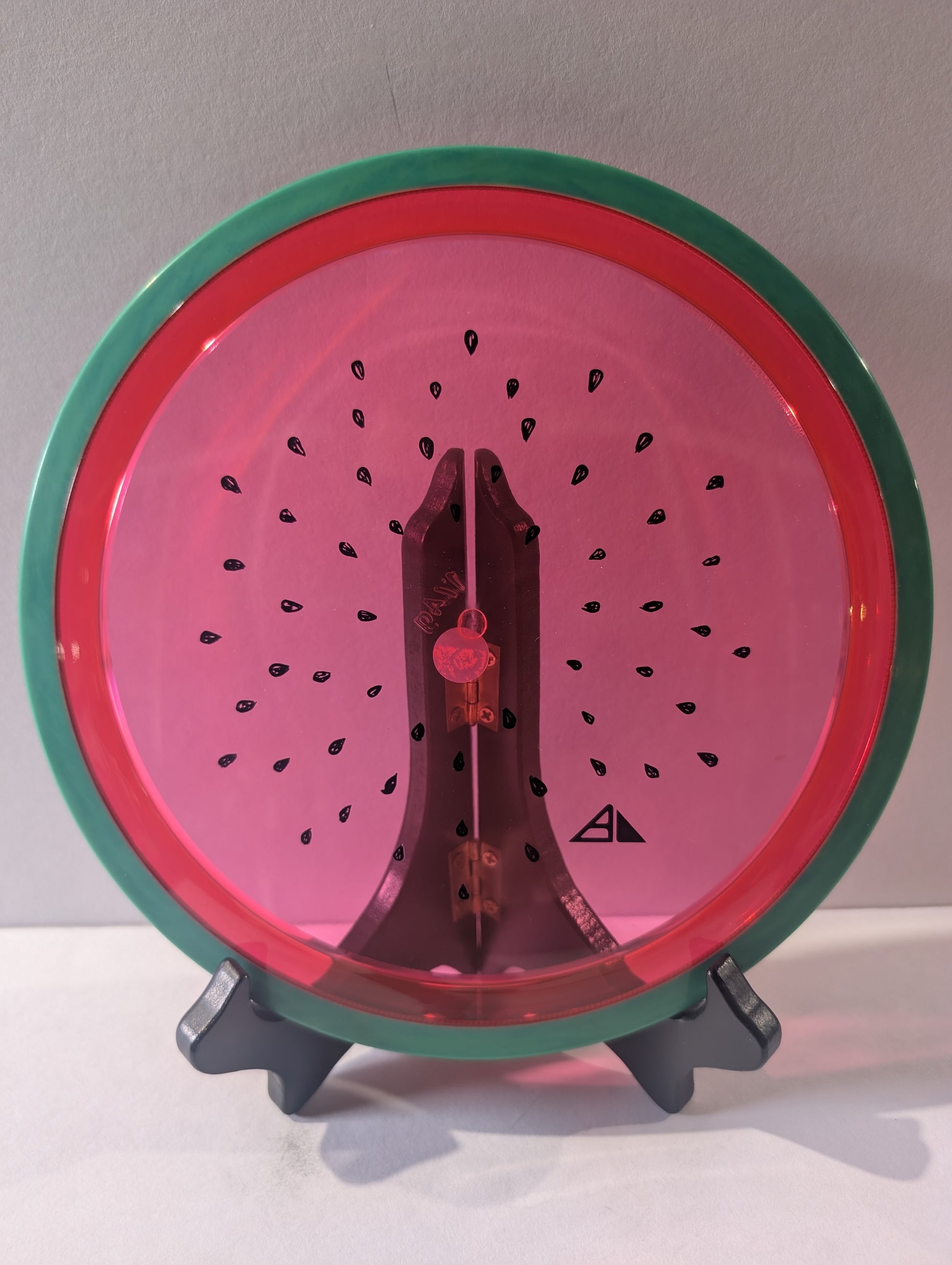 Watermelon disc colored like a watermelon with a stand on a plain background