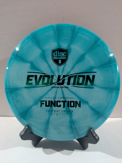 A turquoise swirled Discmania Evolution Lux Vapor Function fairway driver disc golf disc on a black display stand against a neutral gray background.