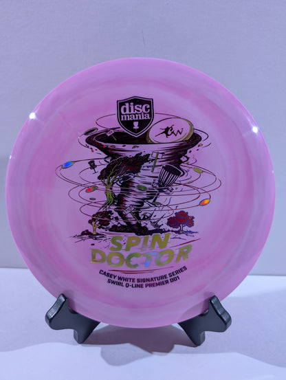A purple Discmania 'Spin Doctor' disc golf disc displayed on a black stand against a light gray background.