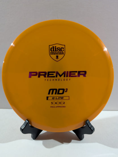 An orange Discmania Premier Technology MD3 Q-Line disc golf disc displayed on a small black stand against a neutral gray background.