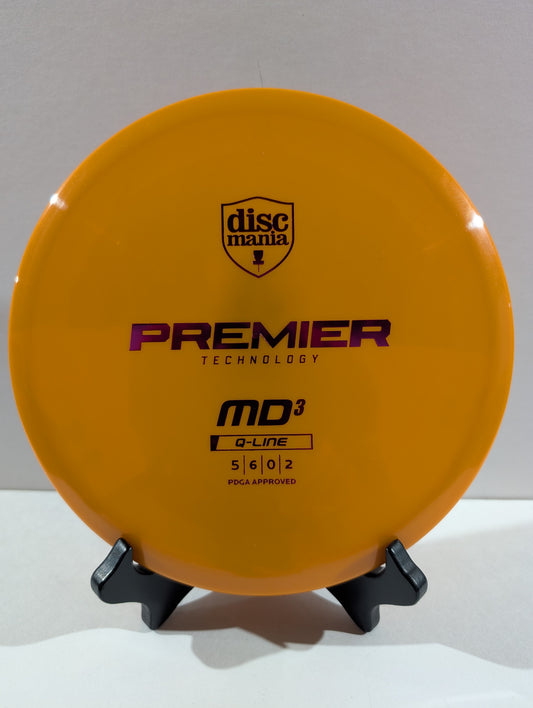 An orange Discmania Premier Technology MD3 Q-Line disc golf disc displayed on a small black stand against a neutral gray background.