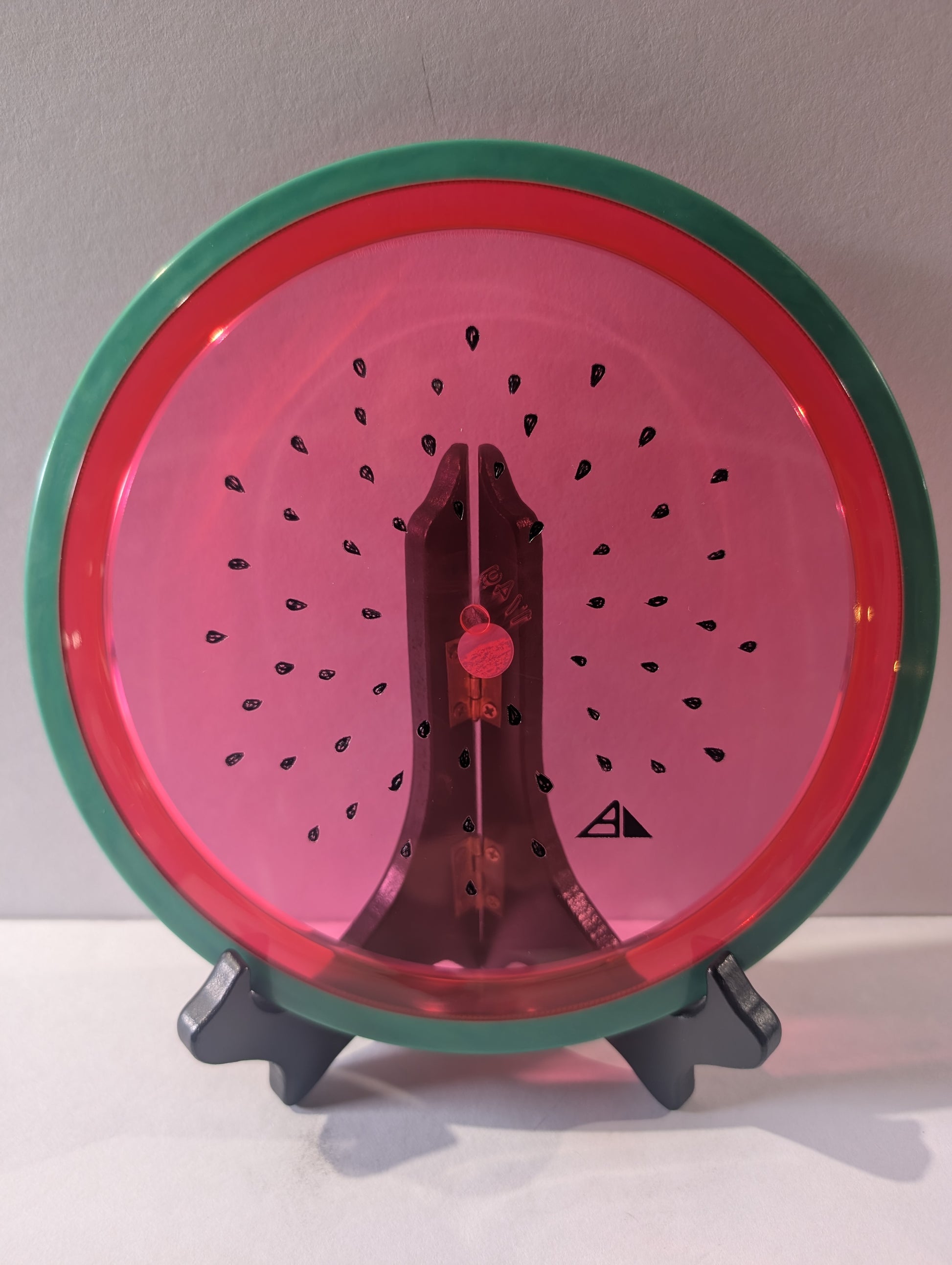 Watermelon disc colored like a watermelon with a stand on a plain background