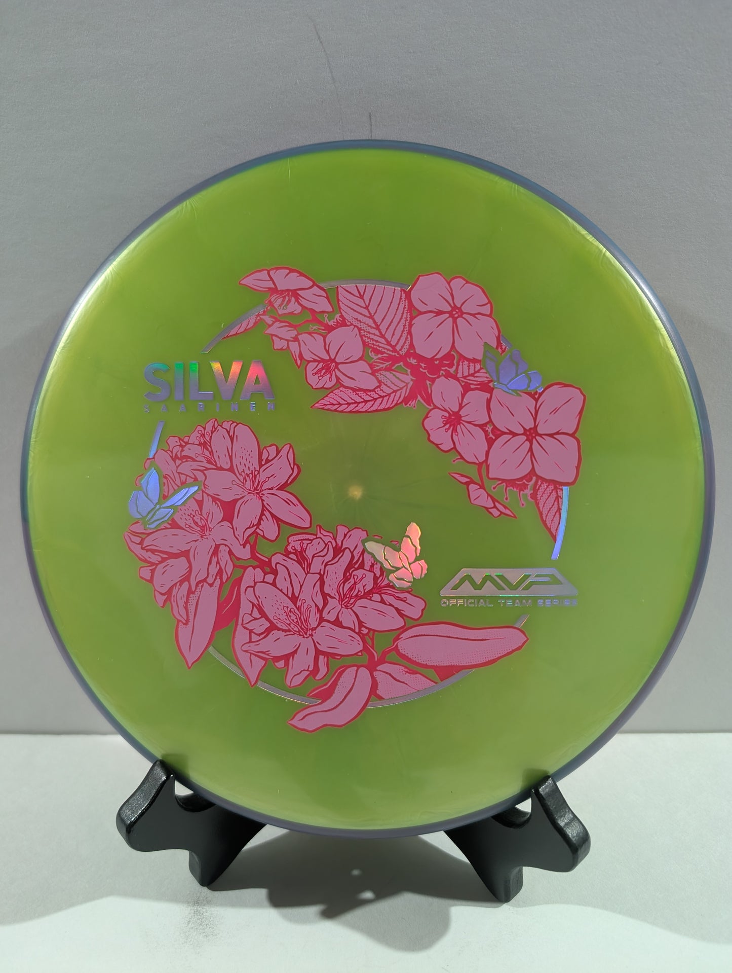 Green disc with pink floral design and 'Silva' branding on a stand against a white background