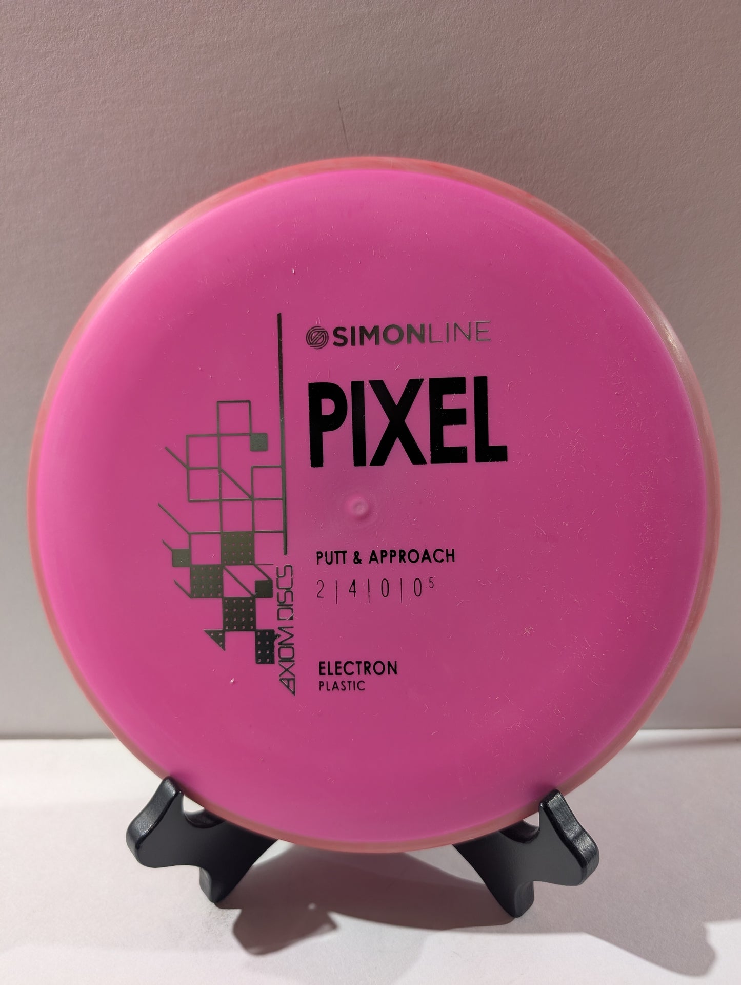 Pink disc golf disc with 'Simonline Pixel' branding on a stand against a neutral background