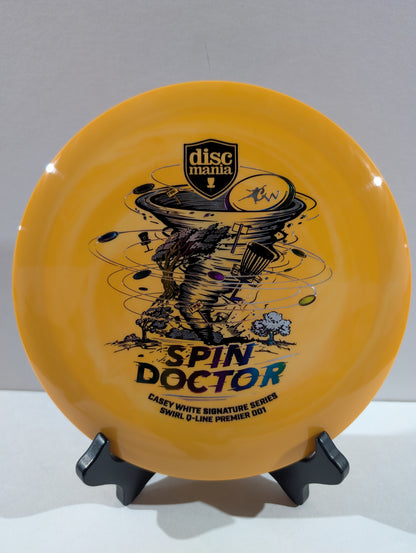 An orange Discmania Spin Doctor flying disc displayed on a small black stand against a neutral gray background.