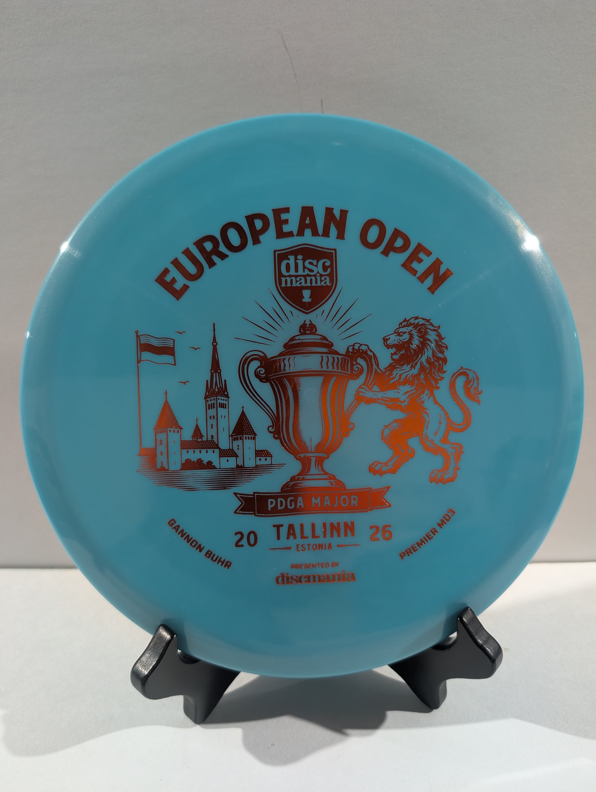 A light blue Discmania European Open disc golf disc displayed on a small black stand against a neutral light gray background.