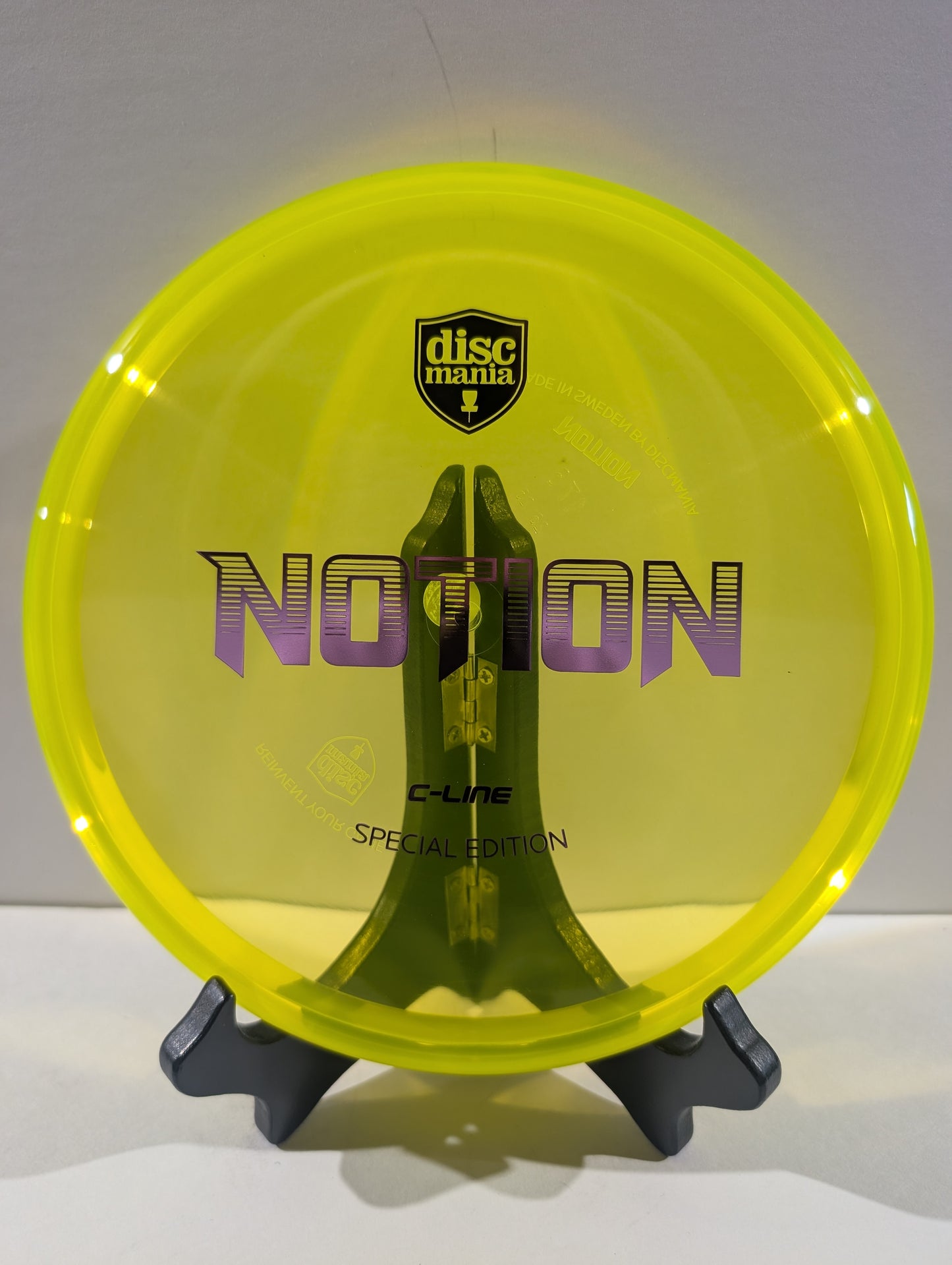 A translucent neon yellow Discmania C-Line Notion Special Edition disc golf disc displayed on a black stand against a neutral gray background.