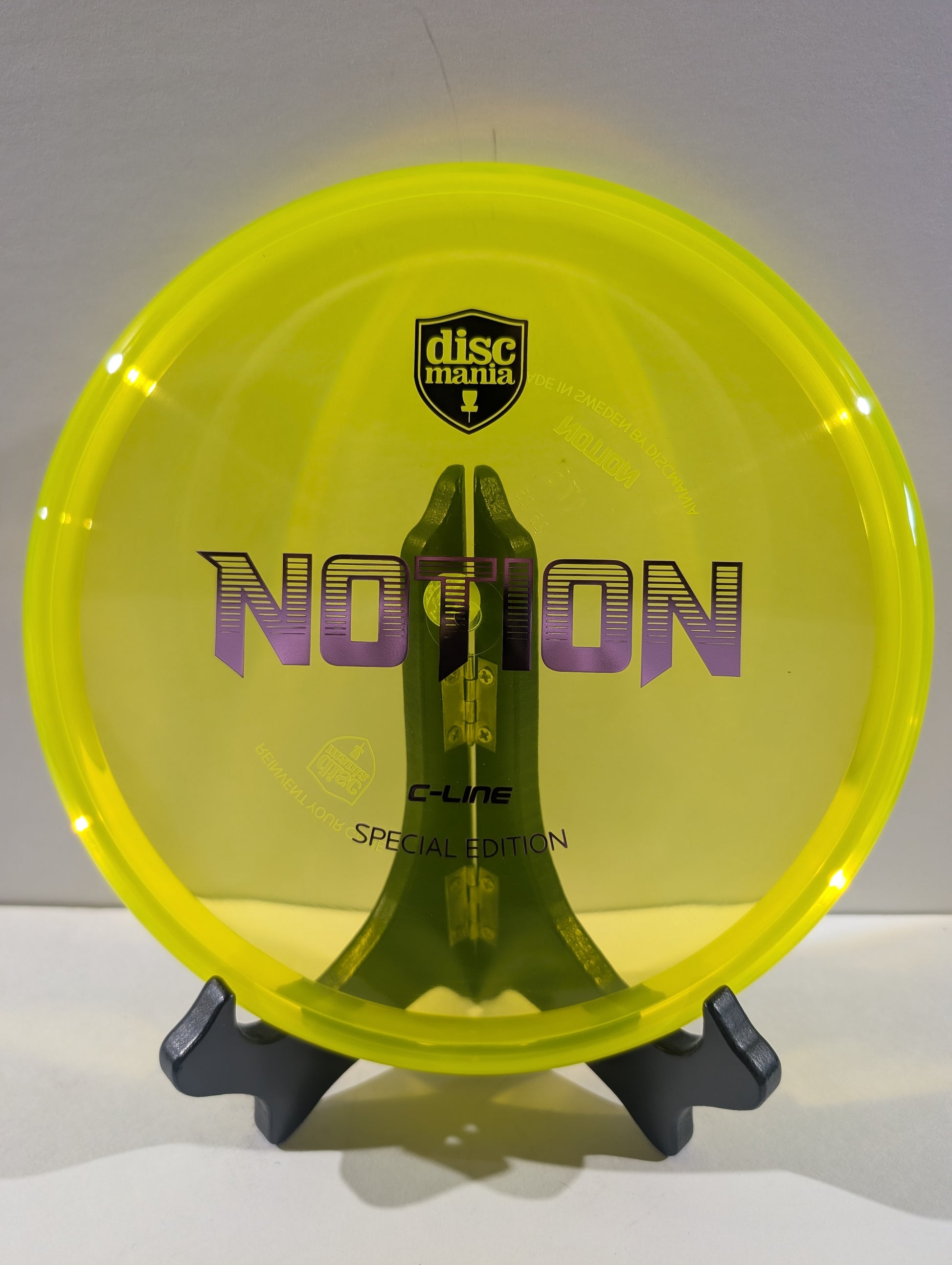 A translucent neon yellow Discmania C-Line Notion Special Edition disc golf disc displayed on a black stand against a neutral gray background.